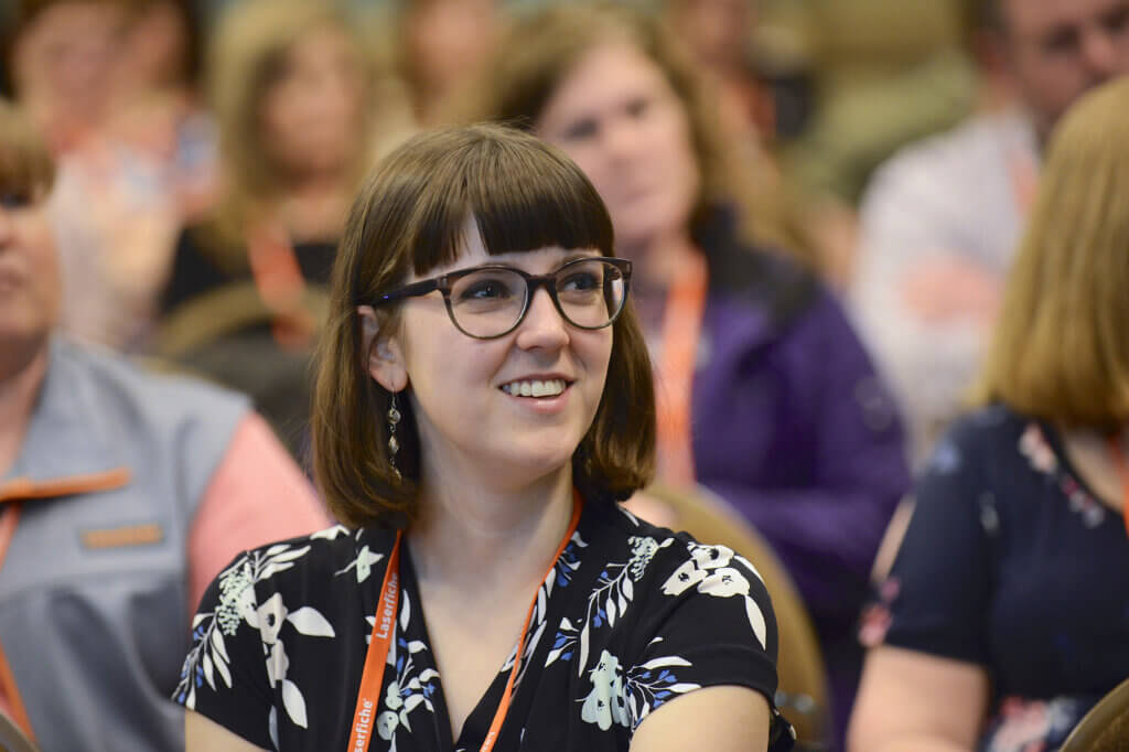Woman smiling in audience at technology conference.